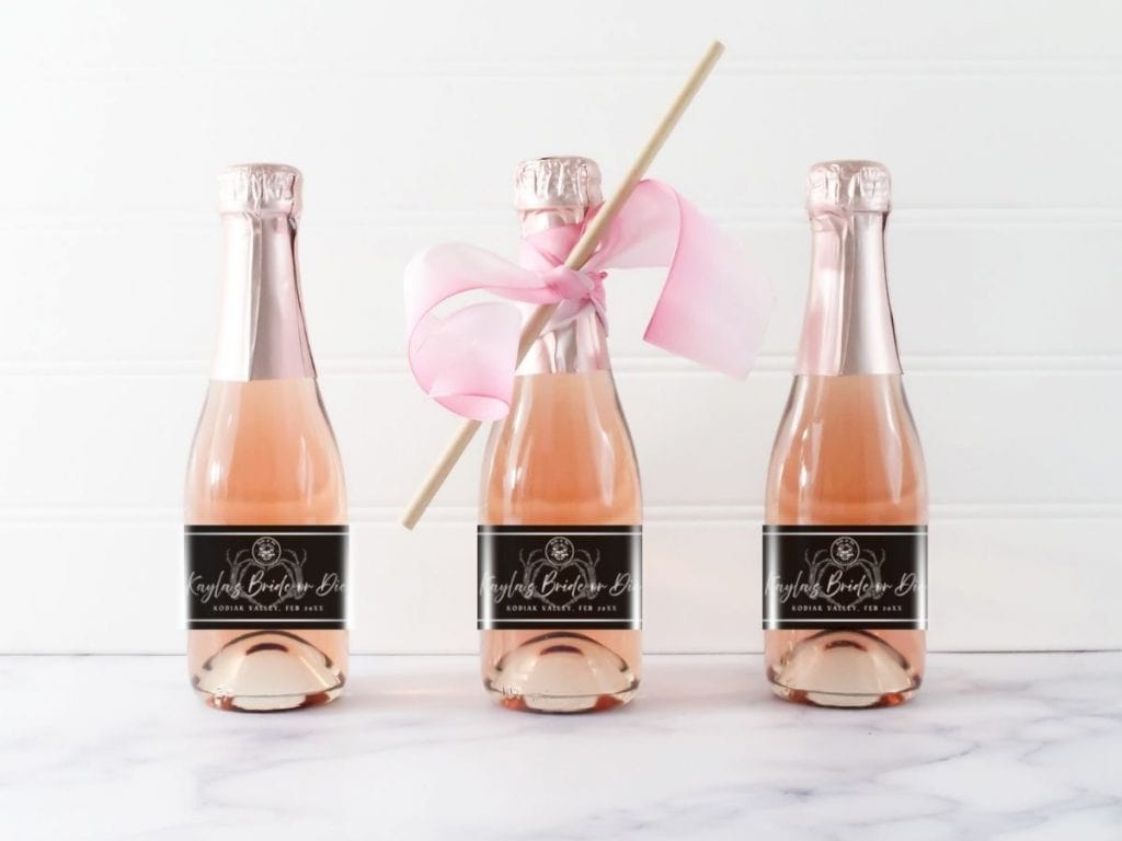 Sparkling rosé champagne bottles with custom wedding labels, decorative pink ribbon, and a pink party pick.