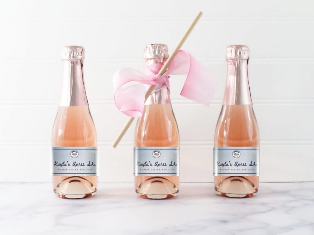 Bubbly pink champagne bottles with personalized labels and a pink ribbon-wrapped straw.