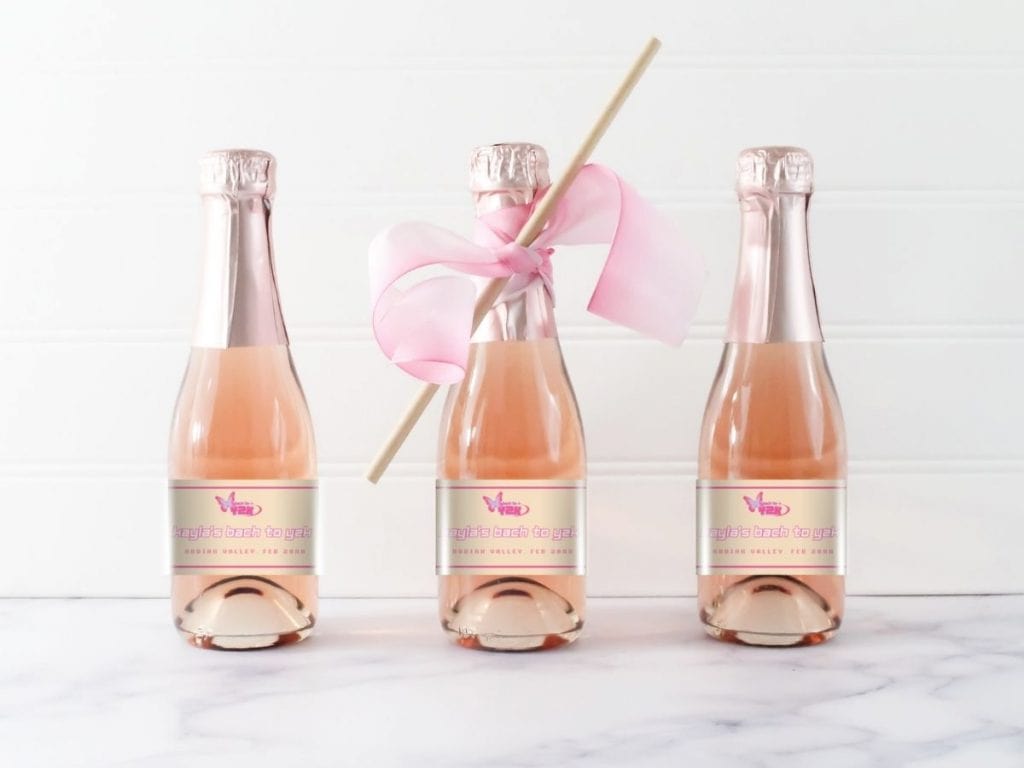 Pink champagne bottles with custom y2k bachelorette labels and a festive pink ribbon, perfect for a celebration or special event.